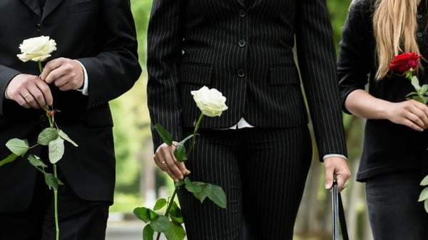 Three people at a funeral wearing black suits