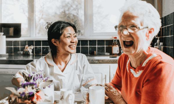 Senior lady laughing in kitchen with her carer